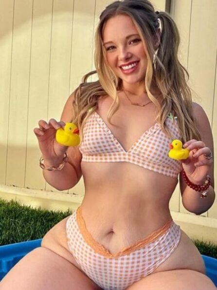 Bikini-clad woman holding yellow ducks in a pool, smiling, grassy outdoor setting.