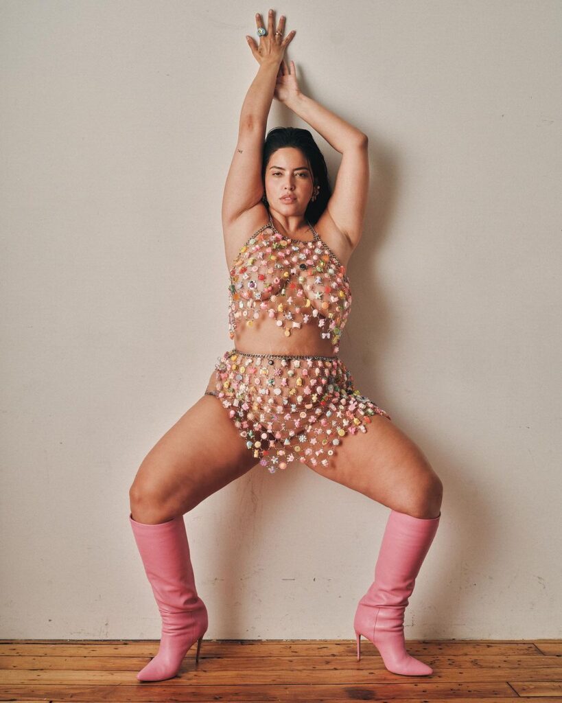 A woman wearing a garment poses indoors for a photo shoot. Focus on her clothing, legs, and waist. She appears to be a dancer or model showcasing choreography.