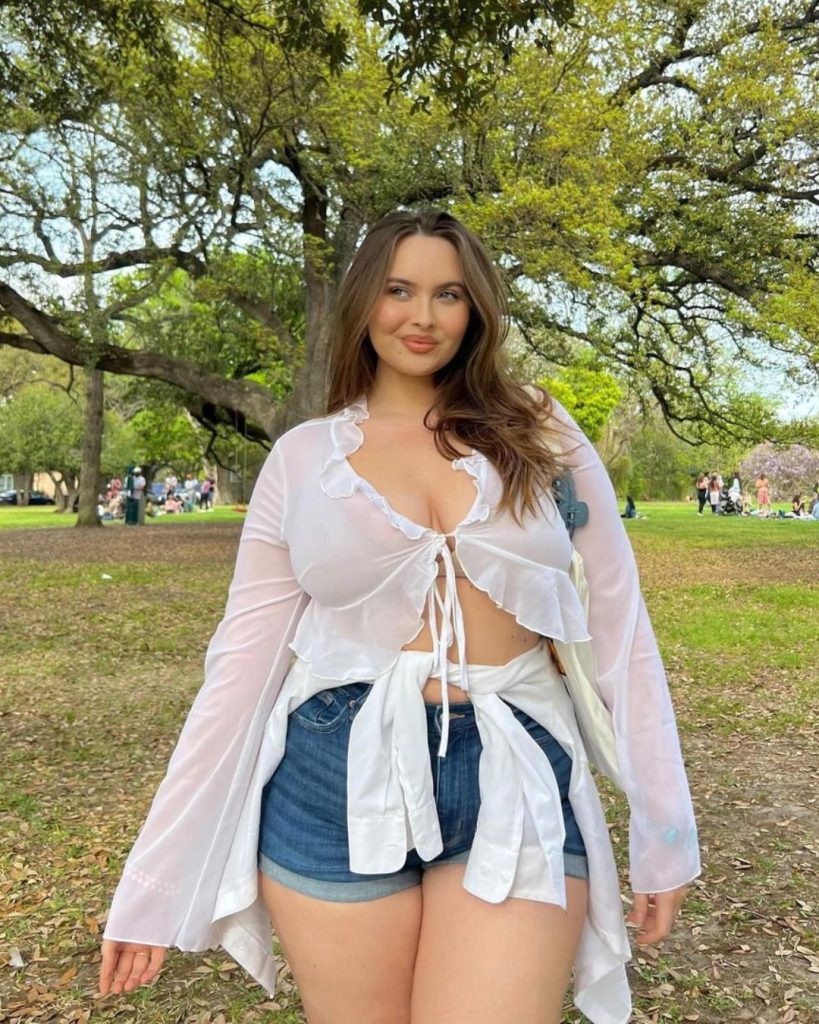 A woman in a white shirt and denim shorts, looking fabulous in a park with a blue skirt.