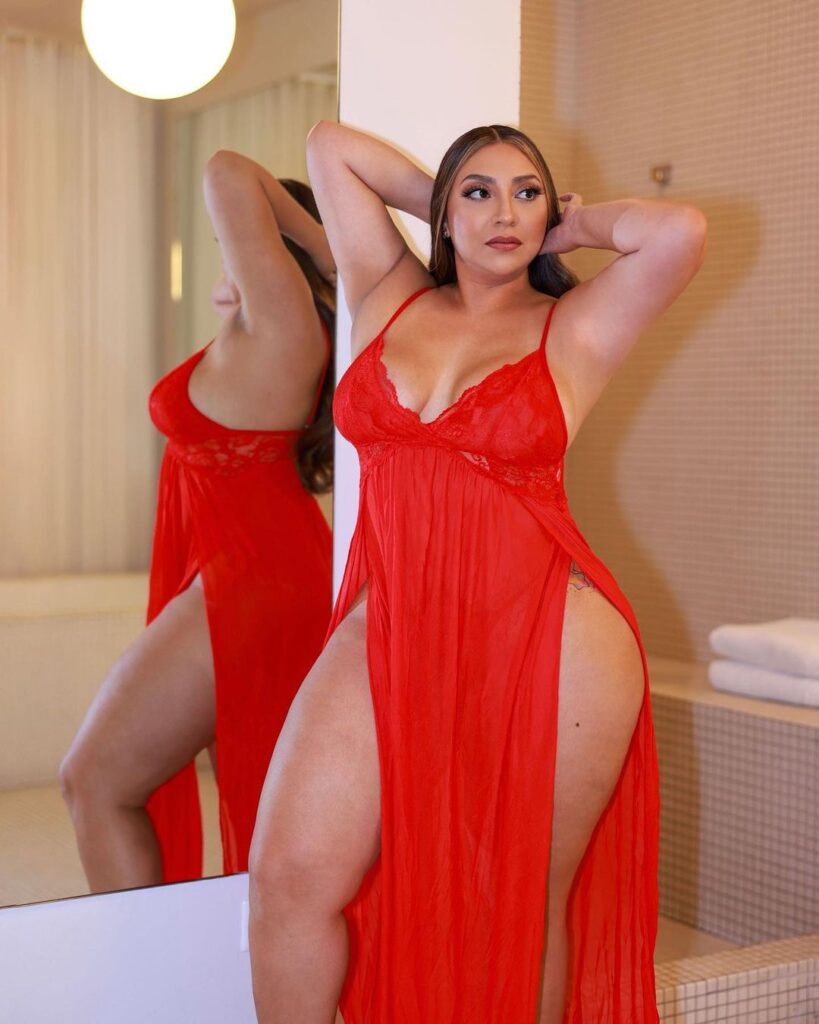 A woman in a red dress smiling for a photo shoot indoors. The image shows her face, abdomen, shoulders, waist, and thighs.