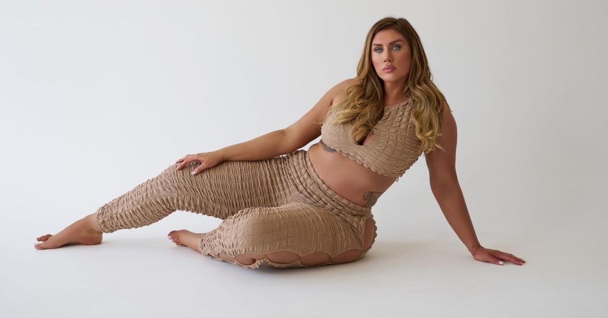 Model in dress posing indoors against wall, emphasizing clothing, face, thigh, stomach, knee, and hip in a balanced pose.