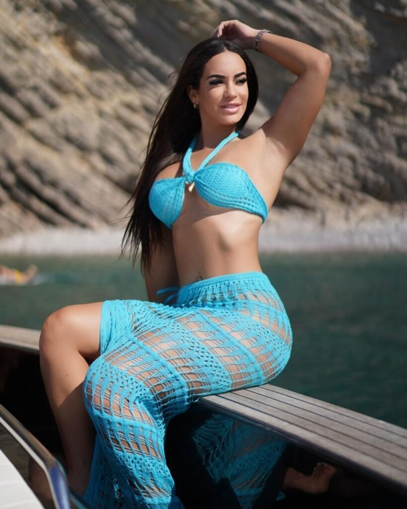 Image of woman in blue bikini and skirt sitting on boat, showcasing swimwear fashion by water.