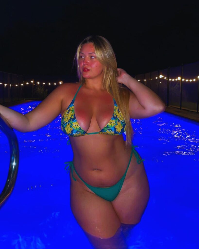A woman in a bikini enjoying herself in a pool, wearing swimwear and smiling. Tags: swimwear, bikini, lingerie, outdoor.