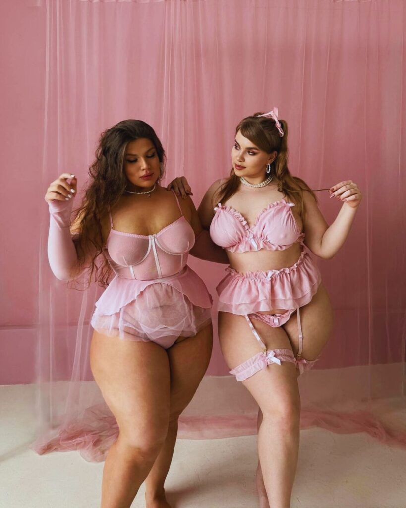 Two women in pink lingerie smiling at the camera.