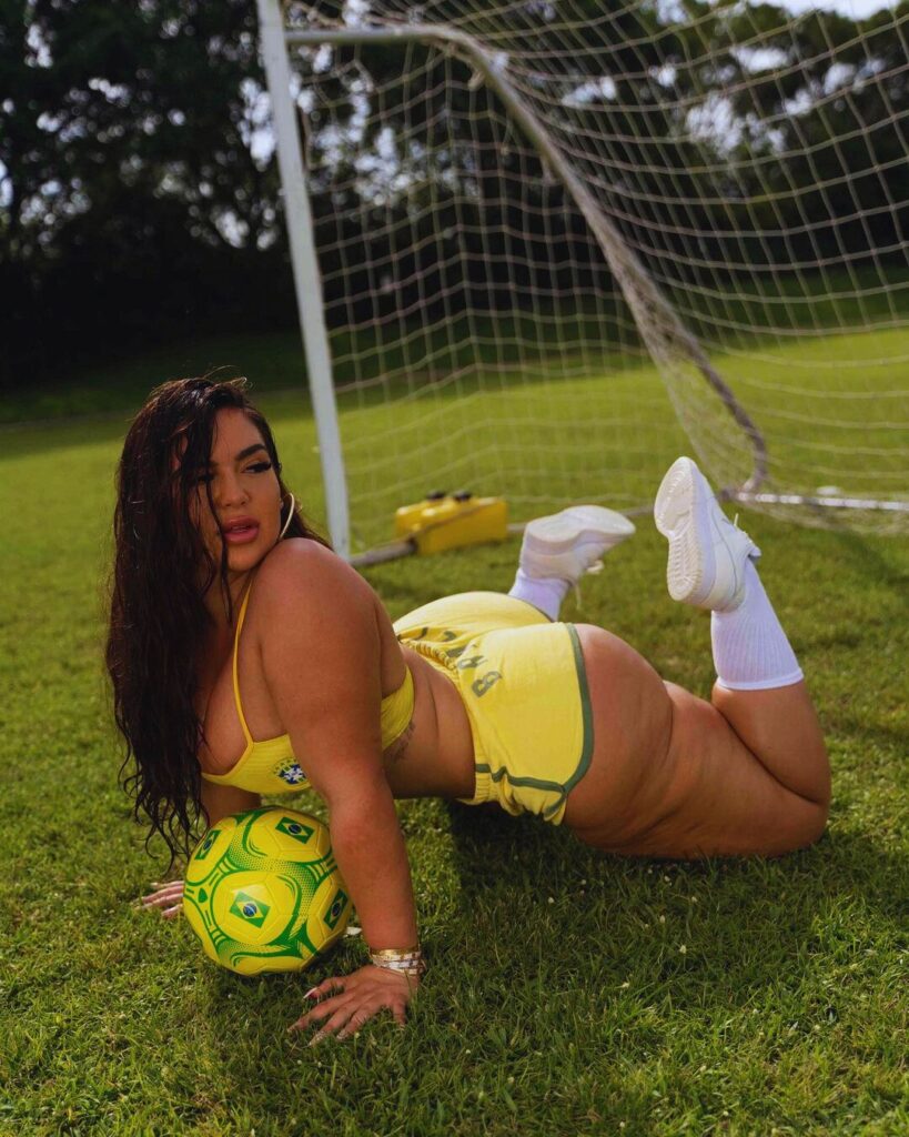 A girl in a yellow bikini enjoying the outdoors, lying on the grass with a soccer ball nearby.