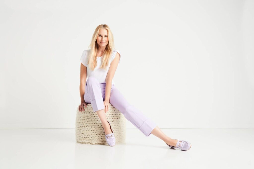 Woman sitting on wicker basket in purple pants.